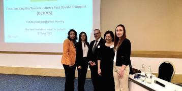 Five people standing in a room with a desk and chair in front of a wall with a projection presentation displayed (Left to right: Marie Fleur Gauci, and Kim Vella from the Ministry for Tourism, Charles Yousif, Anne Marie Thake and Krista Rizzo from the University of Malta)